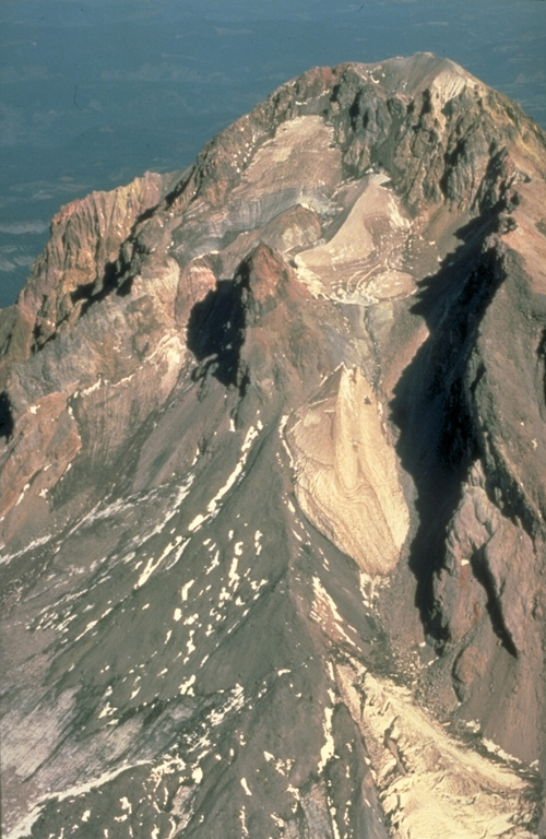 This aerial view of Mount Hood from the south shows the Crater Rock lava dome remnants in the center of the photo. The 400-m-wide, 170-m-high Crater Rock dome erupted around 1780 CE and produced block-and-ash flows and resulted in lahars during episodic dome growth. Deposits are distributed along the Sandy River and White River drainages. Photo by Willie Scott, 1990 (U.S. Geological Survey).