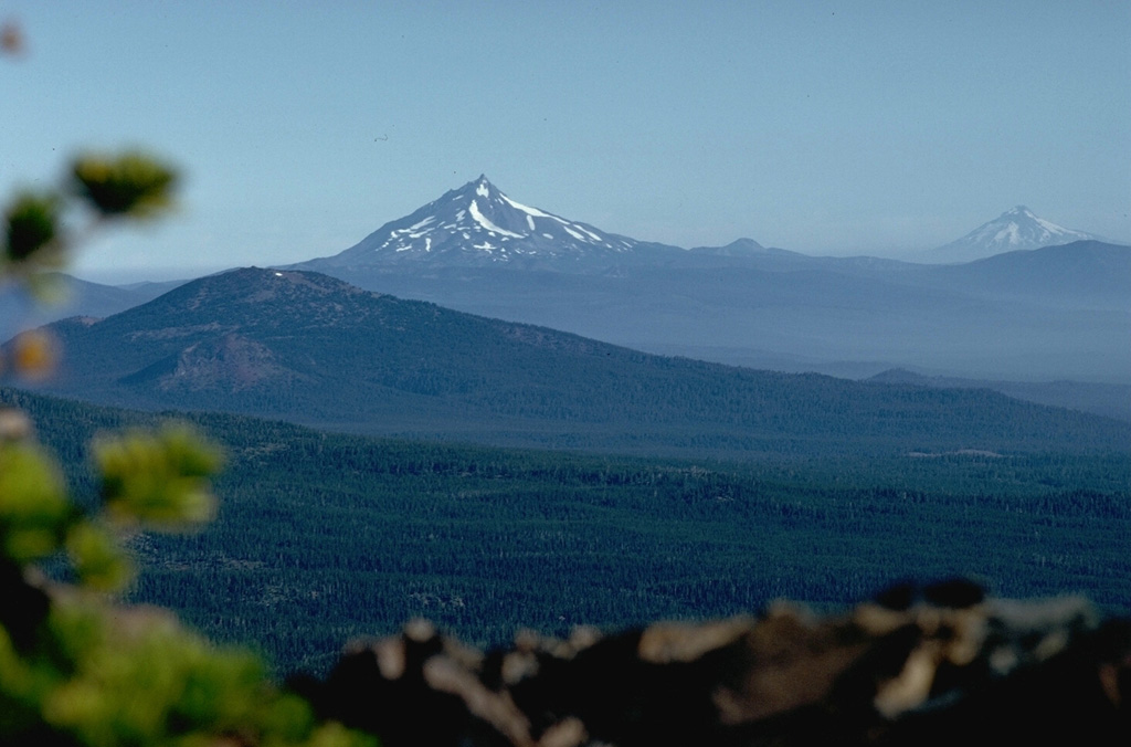 Mount Jefferson in the center and Mount Hood to the right, seen from Broken Top volcano to the south, are the two highest peaks in Oregon, towering above lower volcanic peaks of the High Cascades, such as Black Butte in the foreground. Mount Hood has been active in historical time and Mount Jefferson has Holocene scoria cones to its south, although previous eruptions of the main edifice occurred during the late Pleistocene. Photo by Lee Siebert, 1982 (Smithsonian Institution).