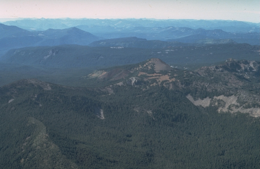 South Cinder Peak, the unvegetated scoria cone near the center of the photo, is the youngest volcanic feature in the Mount Jefferson area. A smaller cinder cone seen at the left on its south flank in this view from the SE, formed about 1,000 years ago and produced a lava flow that traveled to the west. Photo by Dan Miller, 1977 (U.S. Geological Survey).