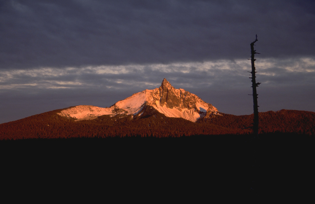 Early morning alpenglow gilds the summit of Mount Washington, one of the most distinctive landmarks of the central Oregon Cascades.  Mount Washington is an extensively eroded basaltic shield volcano capped by a steep-sided central plug.  The central edifice has not been active since the late Pleistocene, but a series of small spatter cones on its NE flank about 4 km from the summit erupted some 1300 years ago. Photo by Lee Siebert, 1995 (Smithsonian Institution).