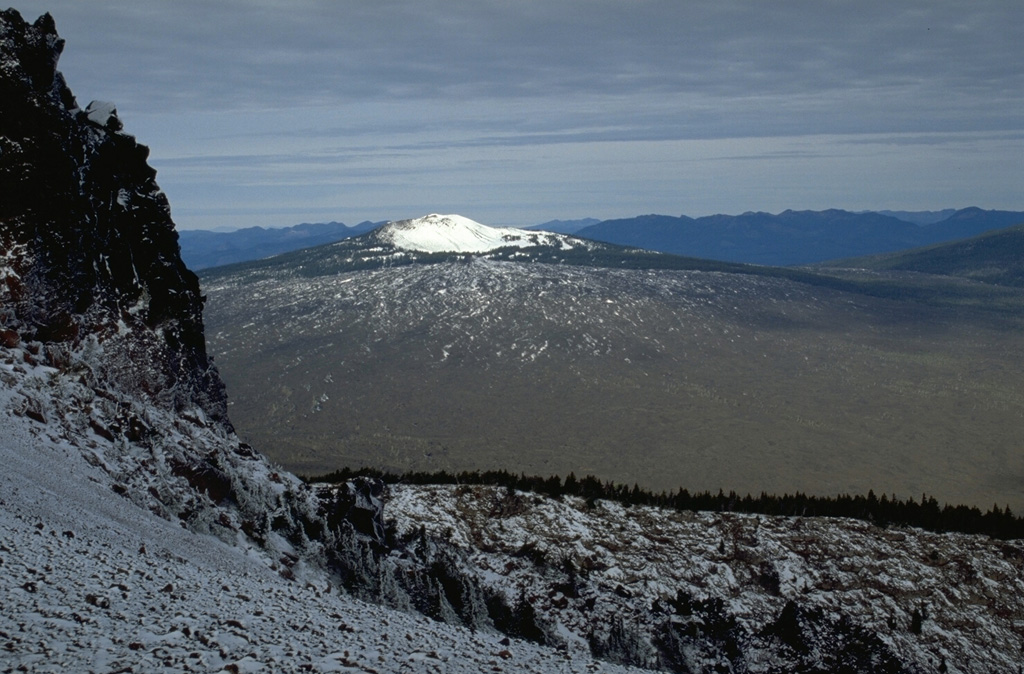 The McKenzie Pass area in the central Oregon Cascades contains one of the largest concentrations of recent volcanism in the United States. Belknap shield volcano, seen here from Black Crater to the SE, is capped by a smaller snow-covered cone. Lava flows from Belknap and the smaller Little Belknap shield volcano in front of it cover nearly 100 km2. Most of the largely unvegetated flows were erupted between about 2,900 and 1,500 years ago. Photo by Lee Siebert, 1995 (Smithsonian Institution).