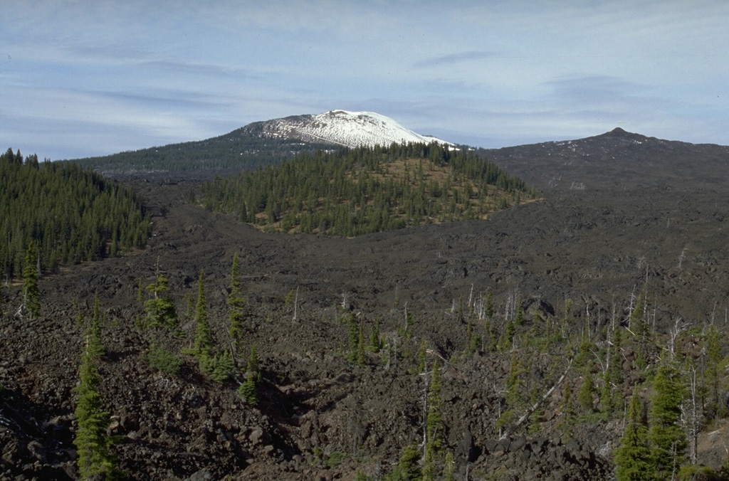 Lava flows from Little Belknap shield volcano in the central Cascade Range of Oregon on the right skyline diverge around a kipuka, a forested island of pre-eruption terrain in the center of the photo. Kipuka is a Hawaiian term for older land surrounded by lava flows.  Photo by Lee Siebert, 1995 (Smithsonian Institution).