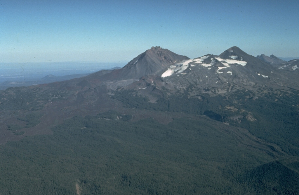 An aerial view from the NW shows North Sister (center) and Middle Sister (right) with young lava flows from N-flank scoria cones. The latest dated lava flow originated about 1,600 years ago from Collier Cone, near the center of the photo below the left flank of North Sister. One lava flow lobe traveled to the NW and levees on the western lobe are visible in the right foreground. They western lobe traveled 13.5 km down the White Branch Creek valley. Photo by Dan Miller, 1977 (U.S. Geological Survey).