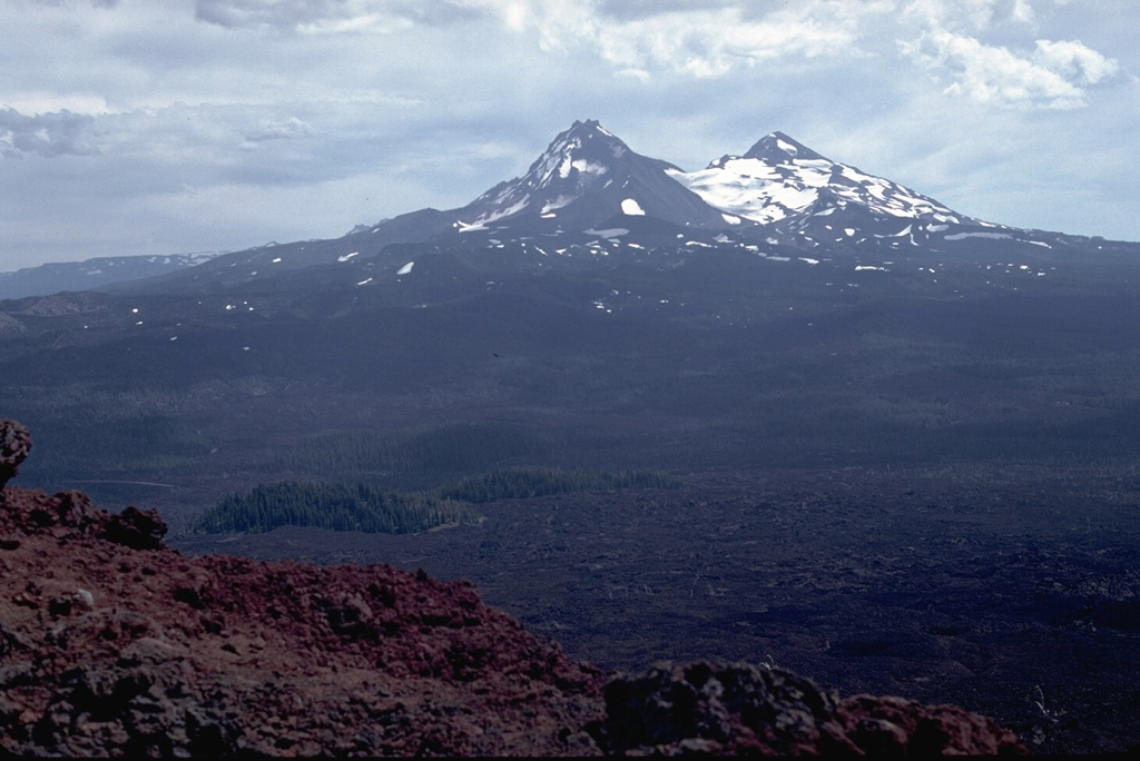 The Belknap Crater scoria cone provides a panorama of recent volcanism in the McKenzie Pass area. Younger lava flows from scoria cones on the north flanks of North and Middle Sister volcanoes in the background merge with flows from the Belknap shield volcano. Most of these flows were erupted in the past few thousand years. In the left foreground, lava flows from Belknap diverge around kipukas, islands of older rocks. Photo by Lee Siebert, 1982 (Smithsonian Institution).
