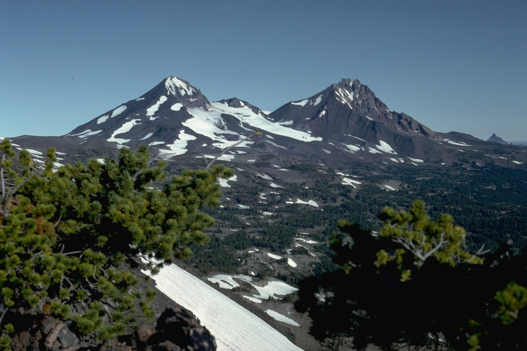 North Sister volcano to the right and Middle Sister to the left, seen from Broken Top volcano to the south, are the two northernmost volcanoes in the Three Sisters volcano group in the central Oregon Cascades. Glaciers have deeply eroded the Pleistocene North Sister volcano, but young Holocene lava flows from scoria cones on the north flank have erupted in the past few thousand years. Photo by Lee Siebert, 1982 (Smithsonian Institution).