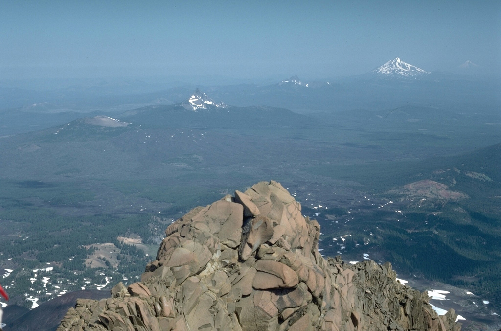 The summit of North Sister provides a panorama of Cascade volcanism that includes, from left to right, lava flows of the McKenzie Pass area in the foreground, the low Belknap shield volcano, the eroded summit pinnacles of Mount Washington and Three Fingered Jack volcanoes, and snow-capped Mount Jefferson to the upper right. Photo by Lee Siebert, 1984 (Smithsonian Institution).