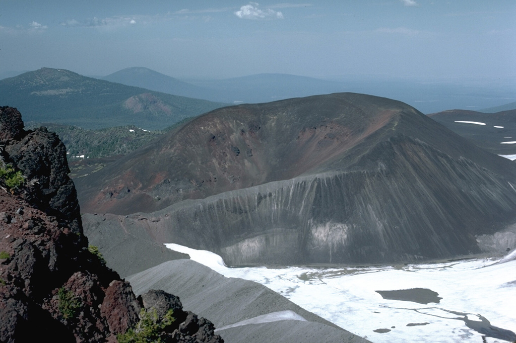 The horseshoe-shaped Collier Cone on the NNW flank of North Sister, partially covered by the Collier Glacier in this 1984 photo, was the source about 1,600 years ago of the youngest dated eruption in the North Sister volcanic field. Lava flows traveled 5 km NW and 13.5 km W down the White Branch Creek. The foreground portion of the cone in this view looking NE has been partially eroded by Collier Glacier when it was at the level of the gray glacial moraine in the foreground on the left margin of the glacier. Photo by Lee Siebert, 1984 (Smithsonian Institution).