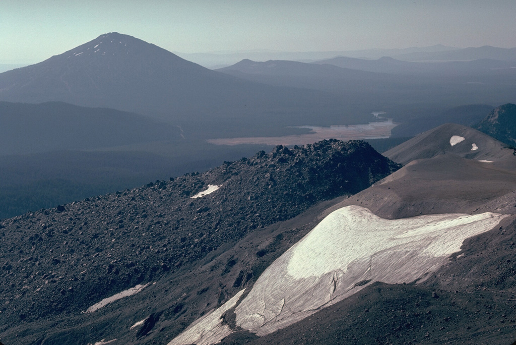 The Newberry lava flow in the foreground is the northernmost and largest of a series of 15 lava domes and flows erupted from a N-S fissure on the SE flank of South Sister volcano. It was preceded by an explosive eruption that produced pyroclastic flows. Another Holocene volcano, Mount Bachelor, is the peak to the left. Photo by Lee Siebert, 1981 (Smithsonian Institution).