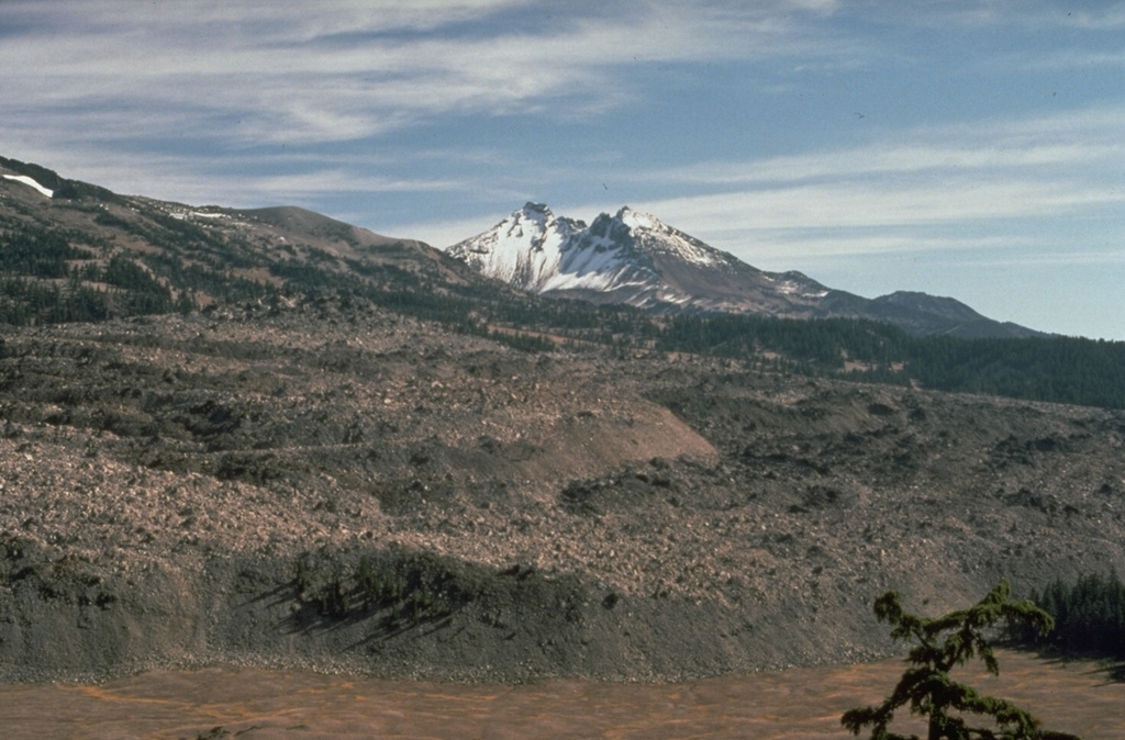 Broken Top volcano provides a backdrop to the margin of the 0.5 km3 Rock Mesa lava flow, which erupted from a vent on the SW flank of South Sister volcano about 2,300 years ago. Emplacement of the lava flow was the final stage of an eruption that began with strong explosions accompanied by pyroclastic flows and surges. Photo by Lyn Topinka, 1985 (U.S. Geological Survey).