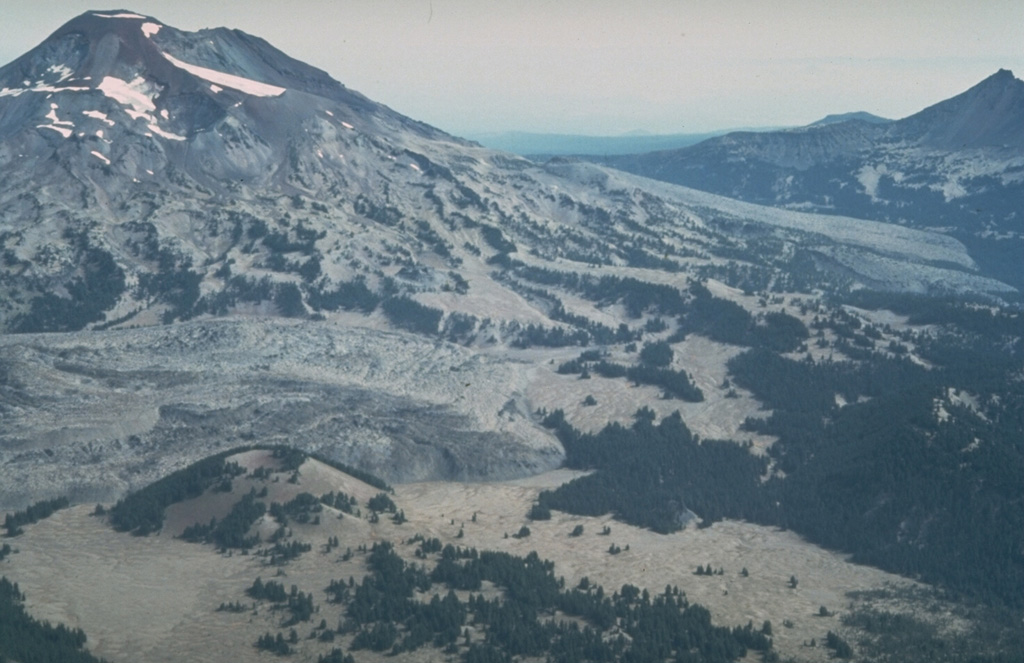 An aerial view from the SW with Le Conte crater in the left foreground shows lava flows from two major Holocene flank eruptions of South Sister volcano. The Rock Mesa flow, immediately behind Le Conte crater and the Newberry lava flow on the South Sister lower SE flank, were erupted between about 2,300 and 2,000 years ago. They were also accompanied by explosive eruptions. Photo by Willie Scott, 1981 (U.S. Geological Survey).