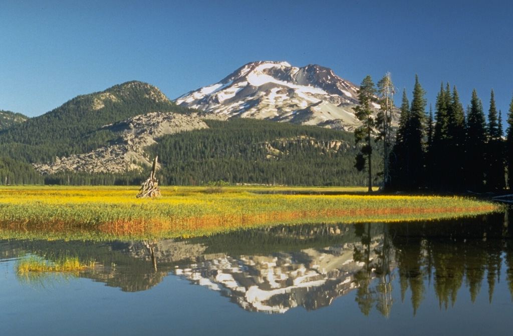 South Sister, reflected in the waters of Sparks Lake, is the highest and youngest of the Three Sisters volcanoes in the central Oregon Cascades. The summit cone of South Sister has not erupted since the late Pleistocene, but the light-colored rocks above the meadow at the left are part of a group of lava flows on the flank that were extruded about 2,000 years ago. Photo by Dave Wieprecht, 1995 (U.S. Geological Survey).