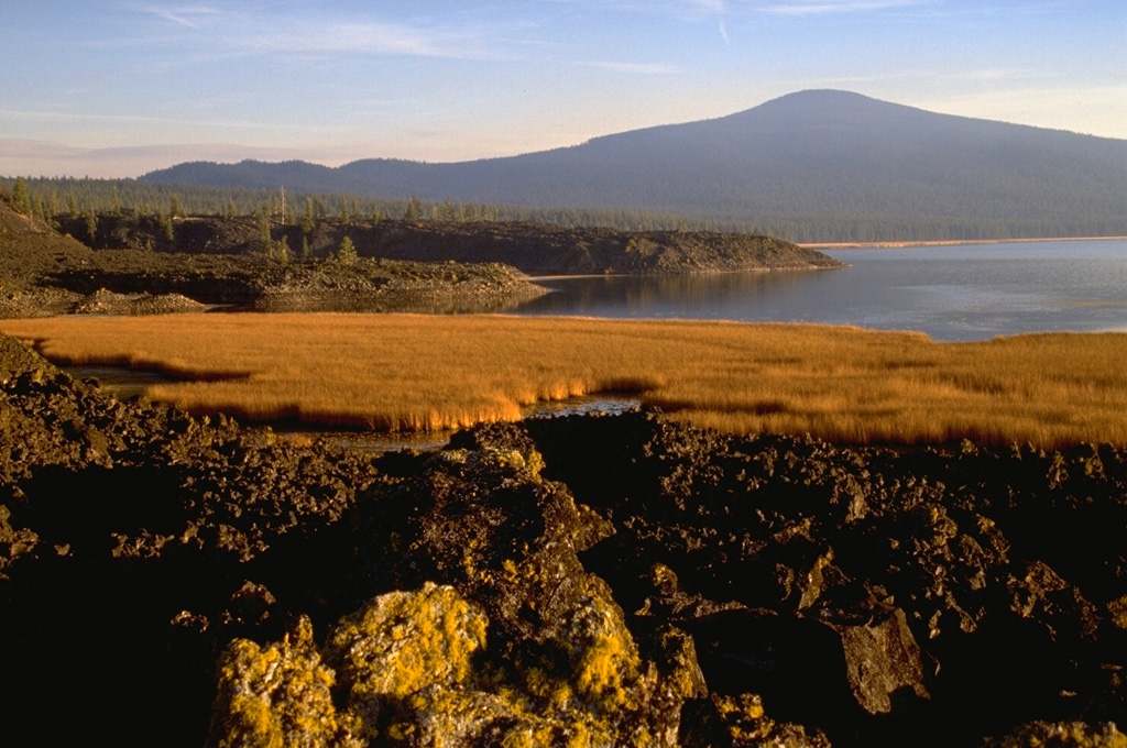 Three small scoria cones oriented along a N-S line produced large andesite lava flows. The northernmost flow formed the natural dam that created Davis Lake (right) and the two other flows are located behind Hamner Butte in the background. The middle flow has been radiocarbon dated to about 5,050-5,600 years old; the other two are considered to have erupted at around the same time and are possibly surface manifestations of the same dike. Photo by Lee Siebert, 1995 (Smithsonian Institution).