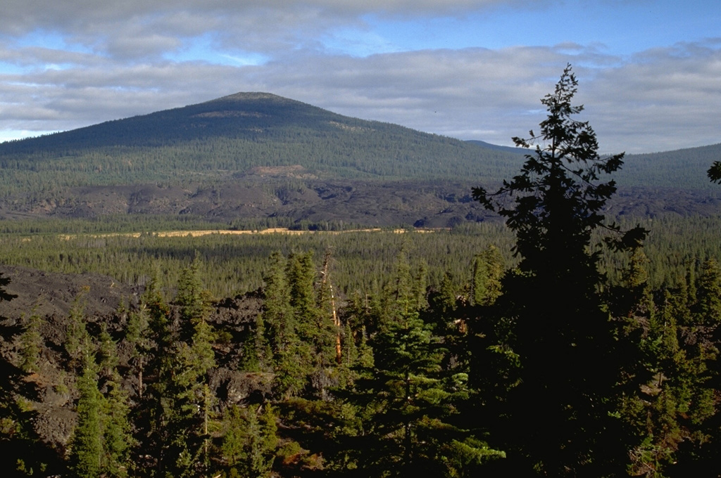 The middle of three scoria cones with associated andesite lava flows near Davis Lake is seen here from Black Rock Butte, which is the southernmost cone, with the Pleistocene Hamner Butte shield volcano in the background. The middle lava flow has an age of 5,050-5,600 years. The vent that produced the middle flow has a flat summit that has been quarried for road aggregate. Photo by Lee Siebert, 1995 (Smithsonian Institution).