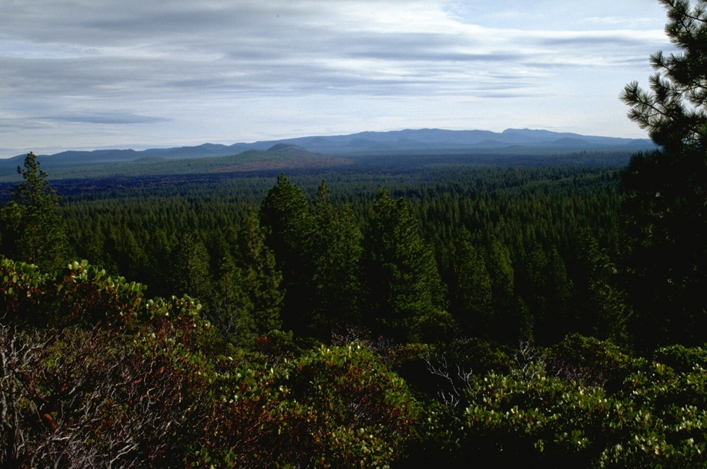 Newberry shield volcano covers an area of about 1,600 km2 about 60 km E of the crest of the Cascade Range in central Oregon. The low-angle shield volcano covers an area of 60 km in a N-S direction and 30 km E-W. More than 400 scoria cones dot the flanks of the volcano, including Lava Butte at the left center of this photo, one of many cones formed around 6,100 years ago along the NW rift zone. Photo by Lee Siebert, 1995 (Smithsonian Institution).