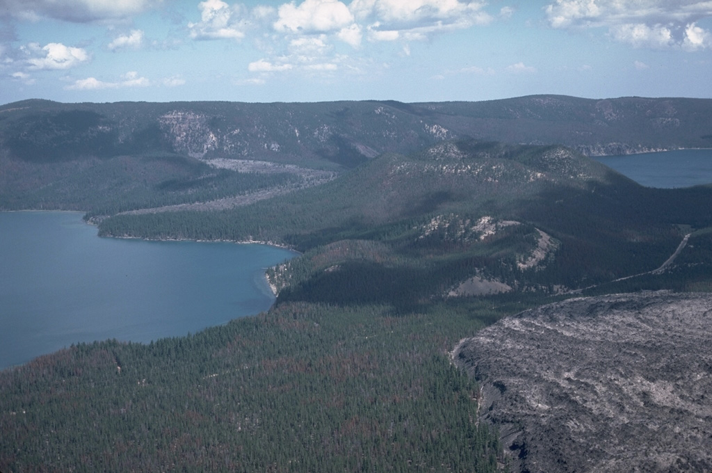 A major eruption about 6,400 years ago produced the large Central Pumice Cone in the center of Newberry caldera, a pumice ring, and obsidian lava flows. The Interlake obsidian flow (on the far side of the left-hand lake, Paulina) originated from a vent on the north caldera wall and flowed onto the caldera floor and divided around Central Pumice Cone. The west lobe (seen here) flowed into Paulina Lake, while the east lobe flowed behind Central Pumice Cone into East Lake. The Game Hut obsidian flow was also erupted at this time. Photo by Lee Siebert, 1984 (Smithsonian Institution).