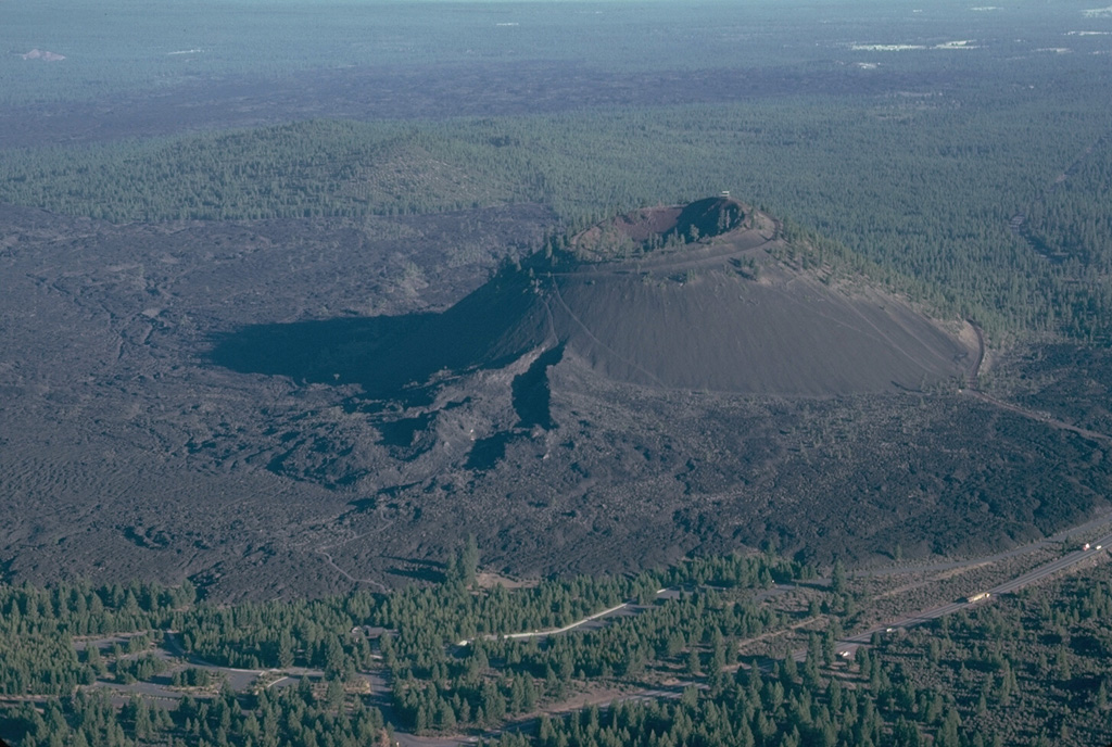 Lava Butte is a scoria cone on the NW flank of Newberry volcano at the end of fissure system that extended from the caldera rim about 7,000 years ago. Following construction of the cone, the SW flank fissure at the base of the cone (in the foreground) fed a voluminous lava flow that traveled to the north and changed the course of the Deschutes River. Photo by Lee Siebert, 1981 (Smithsonian Institution).
