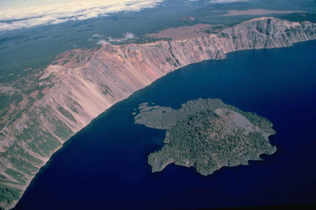 Wizard Island formed within a few hundred years of formation of Crater Lake caldera from a vent near the west caldera rim.  This aerial view from the south shows the island, with a symmetrical cinder cone at its right side and lava flows forming small peninsulas on its flanks.  Hillman Peak, in the center on the caldera rim, is the youngest of the pre-collapse Mount Mazama stratovolcanoes. Copyrighted photo by Katia and Maurice Krafft, 1984.
