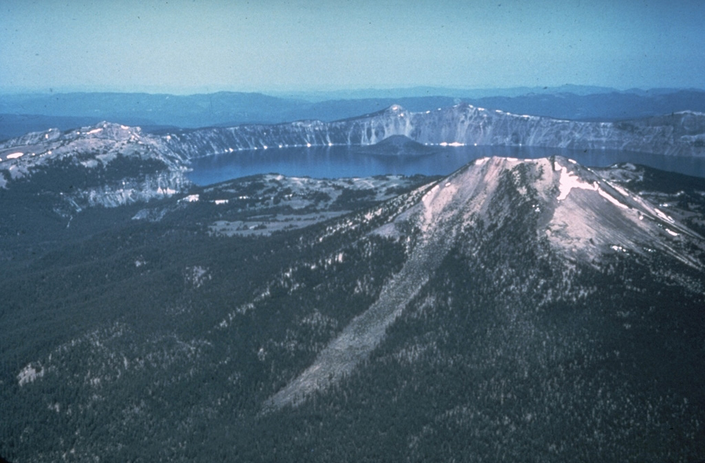 The 8 x 10 km wide Crater Lake caldera formed about 7,700 years ago during one of the world's largest Holocene eruptions. This eruption resulted in the collapse of ancestral Mount Mazama. This view from the east shows Mount Scott in the right foreground, one of the pre-caldera volcanoes. A post-caldera cone, Wizard Island, rises above the far lake surface. Photo by Peter Lipman, 1981 (U.S. Geological Survey).