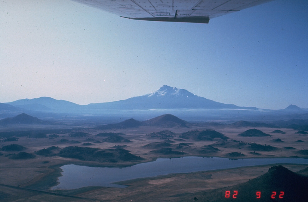 The hilly topography in the foreground is part of the massive debris avalanche deposit produced by collapse of Mount Shasta (center horizon). The roughly 46 km3, rapidly-moving debris avalanche swept some 50 km N. The hummocky area represents relatively intact segments of the volcano that were carried within a more fluidized, mixed bulk of the avalanche. Individual hummocks range up to a few hundred meters in height and roughly 1 km in length. Photo by Harry Glicken, 1982 (U.S. Geological Survey).