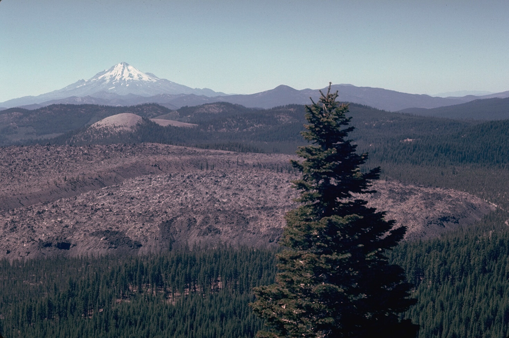 The Little Glass Mountain obsidian flow is seen from Little Mount Hoffman on the western rim of Medicine Lake caldera with Mount Shasta in the background. The flow was erupted on the SW flank of Medicine Lake volcano a little more than 950 years ago. The light-colored rounded peak in line with Mount Shasta is Pumice Stone Mountain, which is overlain by pumice from the Little Glass Mountain eruption. A series of smaller flows to the NE known as the Crater Glass Flows were erupted at about the same time. Photo by Lee Siebert, 1981 (Smithsonian Institution).