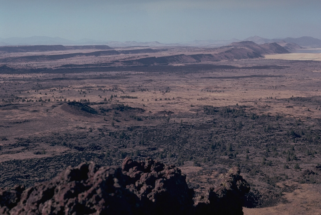 The summit of Schonchin Butte in Lava Beds National Monument provides a view of step-like Basin-and-Range faulting to the NW. The dark lava flow at the base of the closest scarp is the late-Pleistocene Devils Homestead lava flow. Parallel to, and just in front, of that are 3,000-year-old lava flows from fissures at Black Crater and Ross Chimneys. Photo by Lee Siebert, 1981 (Smithsonian Institution).