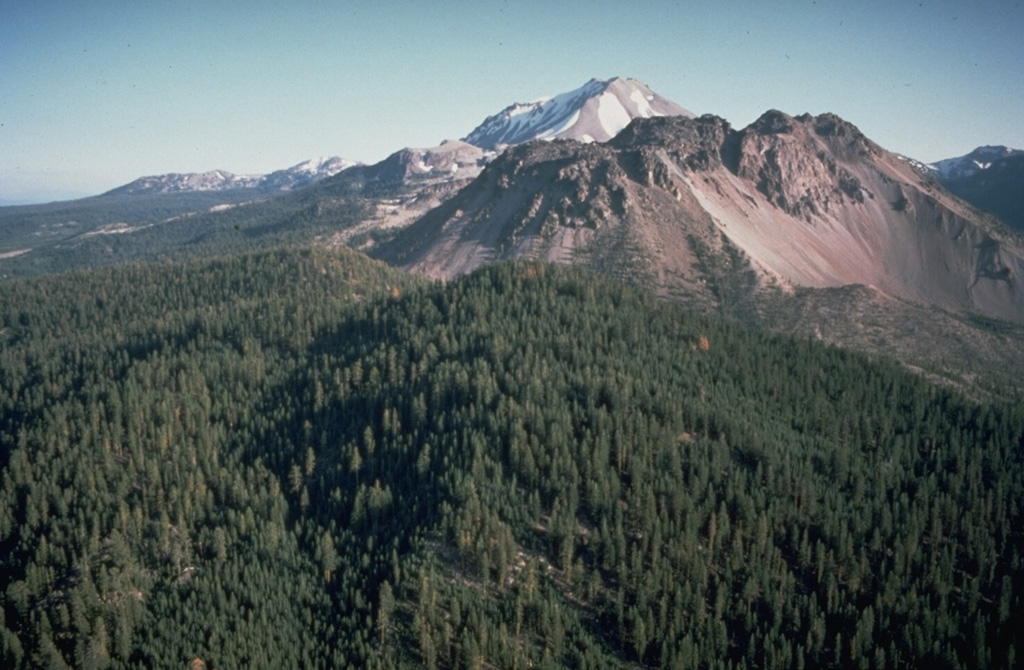 Lassen Peak rises in the background behind the Chaos Crags, a group of dacitic lava domes on Lassen's north flank.  The Chaos Crags were formed during a series of eruptions about 1100 to 1000 years ago in which early explosive eruptions and pyroclastic flows were followed by growth of a complex of five lava domes.  The area of light-colored talus on the right side is the source of a large debris avalanche from Chaos Crags about 1650 CE. Photo by Dan Dzurisin, 1982 (U.S. Geological Survey).