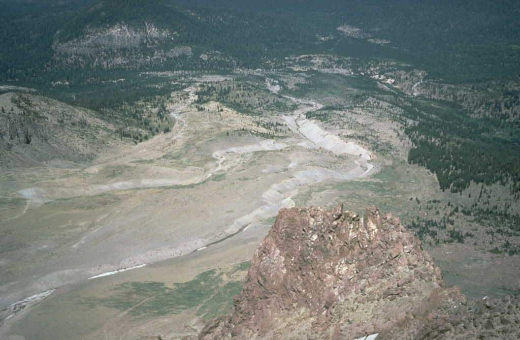 The Devastated Area swept by pyroclastic surges during an explosion on May 22, 1915 is seen here from the NE flank of Lassen Peak.  The May 22 produced an eruption plume as high as 9 km, a pyroclastic surge that swept the area seen here, and a series of three lahars, the two largest of which swept down Lost Creek to the NE.  The area as far as the distant flank of forested Raker Peak at the upper left was affected by the May 22 pyroclastic surge.  Revegetation has begun to cover the distal parts of the May 1915 deposits.   Photo by Bill Chadwick, 1981 (U.S. Geological Survey).