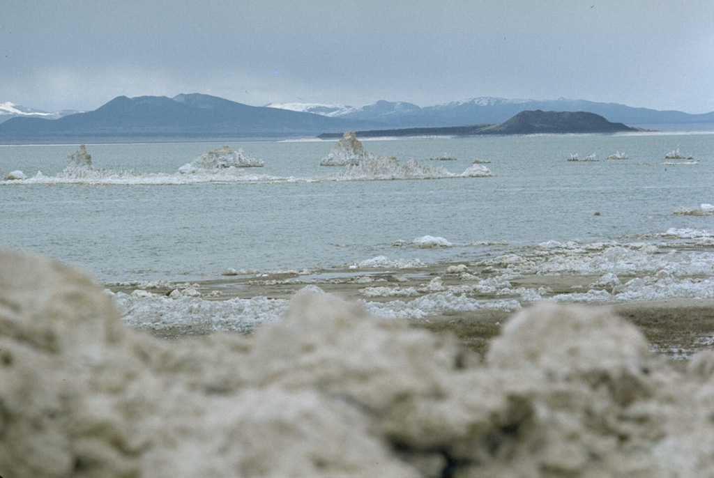 Negit Island, capped by the dark-colored cinder cone at the right, was the source of one of the most recent eruptions of the Mono Lake volcanic field.  Rhyodacitic lava flows overlie a 1240 CE tephra unit.  The light-colored tufa deposits near the western shore of Mono Lake in the foreground were created by deposition of calcium carbonate beneath the waters of the lake. Photo by Lee Siebert, 1973 (Smithsonian Institution).