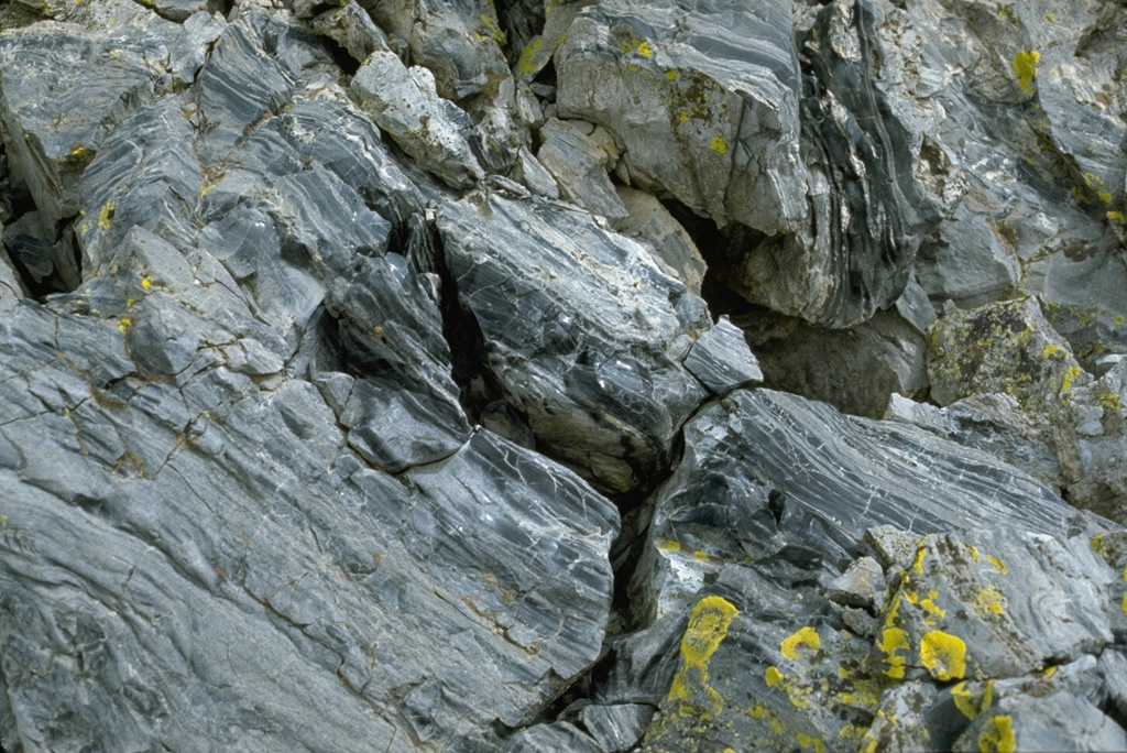 Flow-banded rhyolitic obsidian of the Panum Crater lava dome was erupted about 600 years ago at the northern end of the Mono Craters.  The greenish-yellow areas are lichens on the surface of the dome. Photo by Lee Siebert, 1973 (Smithsonian Institution).