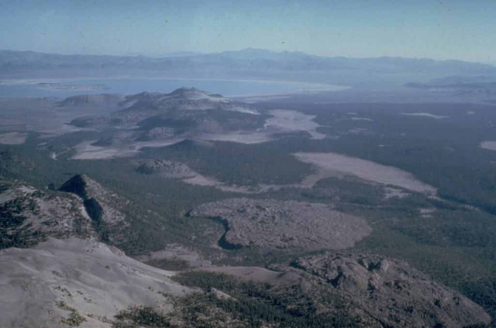 The Mono Craters volcanic field south of Mono Lake at the upper left, is a 17-km-long arcuate chain of rhyolitic lava domes and thick, viscous lava flows.  Mono Craters has been frequently active throughout the Holocene, along with the Inyo Craters chain to the south.  The Inyo Craters chain, which includes the Wilson Butte, Obsidian and Glass Creek domes, which are oriented diagonally along a N-S line from the left center to lower right of the photo.  The latest eruptions of Mono Craters and Inyo Craters occurred nearly simultaneously around 600 years ago. Photo by Roy Bailey, 1980 (U.S. Geological Survey).