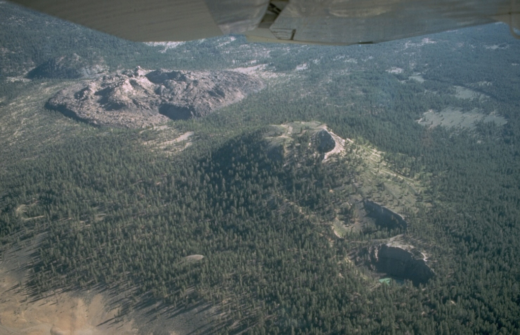An aerial view from the south shows the North and South Inyo Craters phreatic explosion craters diagonally cutting forested Deer Mountain from the right center to lower right, and the unvegetated South Deadman lava dome and obsidian flow and the forested mound of North Deadman dome at the upper left.  Eruption of magmatic tephra and the formation of the phreatic explosion craters preceded emplacement of the lava domes and flows about 600 years ago. Photo by Larry Mastin, 1988 (U.S. Geological Survey).