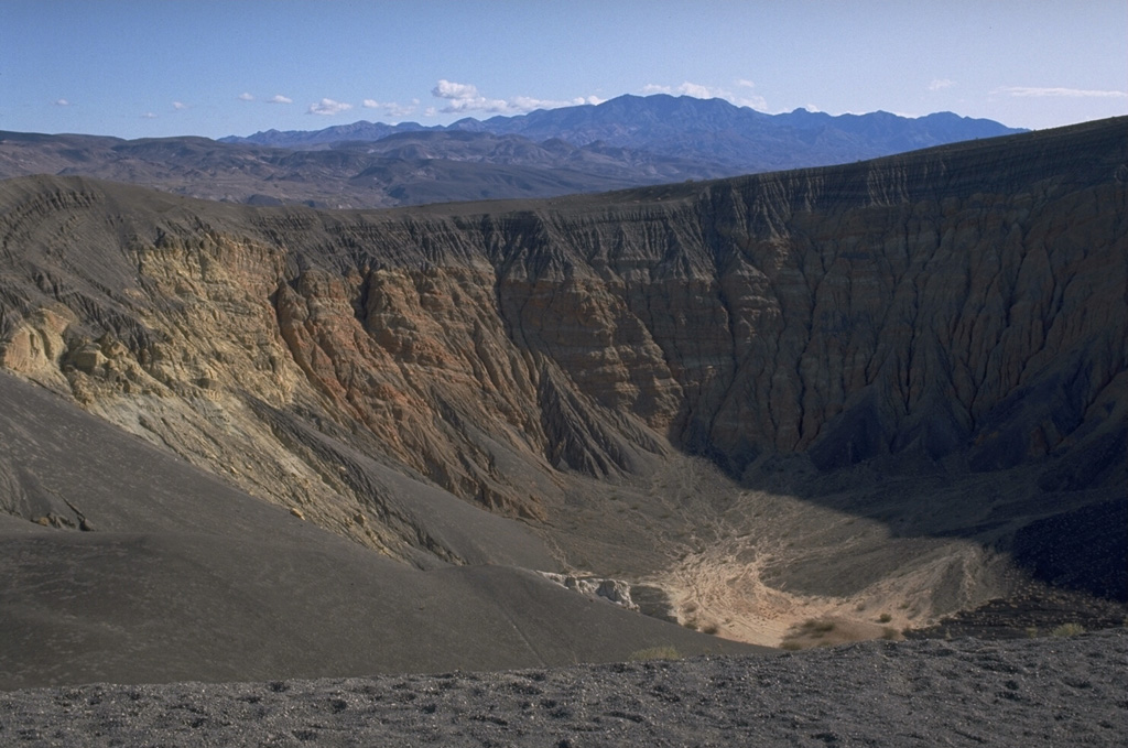 Ubehebe craters are an isolated group of maar volcanoes erupted through nonvolcanic sediments of Death Valley National Park.  The craters were formed by hydrovolcanic explosions along a fault.  The contact between pre-eruption yellowish- and orange-colored sedimentary rocks and overlying black ash deposits from an early stage scoria cone can be seen at the upper part of the western wall of 800-m wide, 235-m deep Ubehebe crater, the youngest and largest crater. Photo by Lee Siebert, 1974 (Smithsonian Institution).