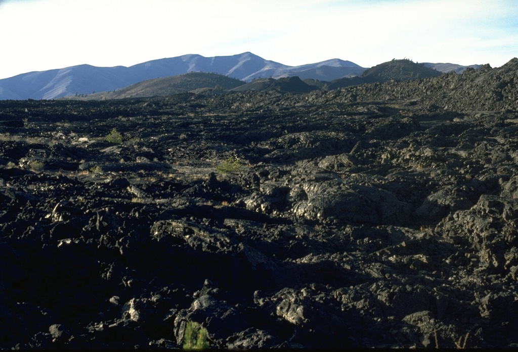 The Blue Dragon lava flow covers about 280 km2 of Craters of the Moon lava field with flat-lying pahoehoe lava.  The 3.4 cu km flow, erupted about 2075 years ago, is the largest in the Craters of the Moon volcanic field.  It traveled up to 25 km to the east and 15 km to the SW from fissure vents near the center of this photo.  The largely pahoehoe lava flow is named for a characteristic iridescent dark- to light-blue, glassy crust. Photo by Lee Siebert. 1994 (Smithsonian Institution).