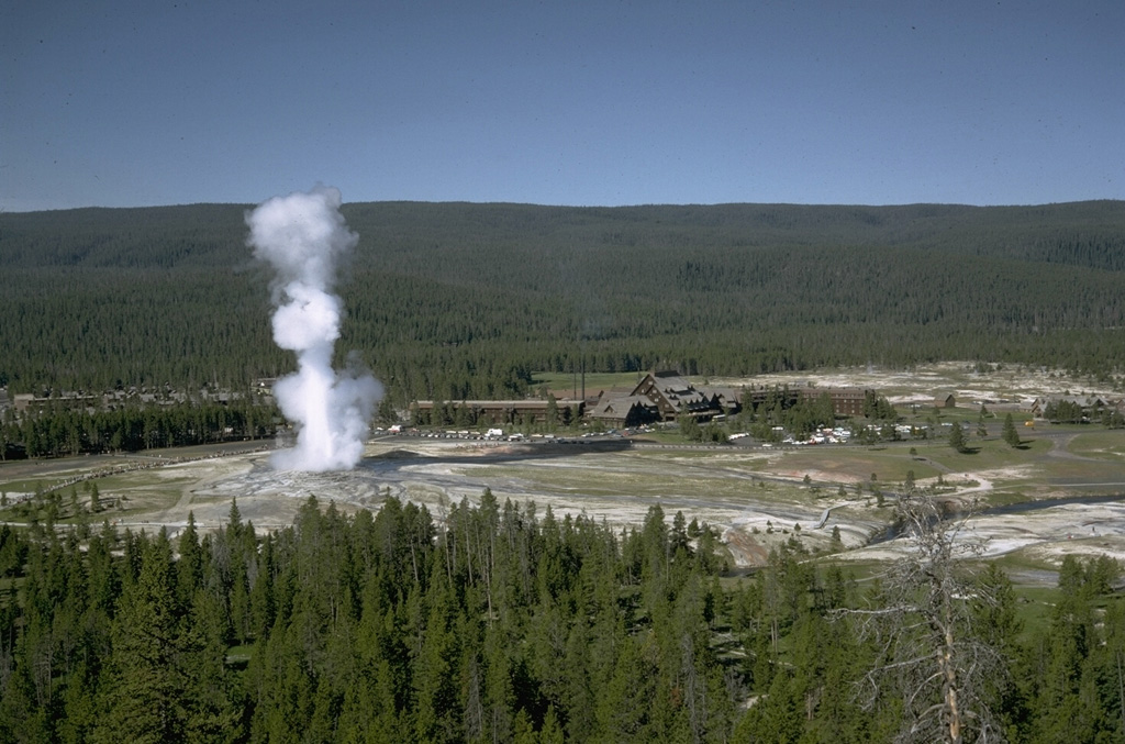 An eruption of Old Faithful, perhaps the world's best known geyser, rises above Yellowstone's Upper Geyser Basin.  Old Faithful is a periodic geyser, with eruptions to heights of about 40 m at intervals of 30 to 100 minutes.  Old Faithful Lodge to the right provides a rustic backdrop to the Upper Geyser Basin, which contains more geysers than are known altogether in the rest of the world.  The forested ridge in the background is underlain by massive post-caldera rhyolitic lava flows of the Madison Plateau. Photo by Lee Siebert, 1968 (Smithsonian Institution).
