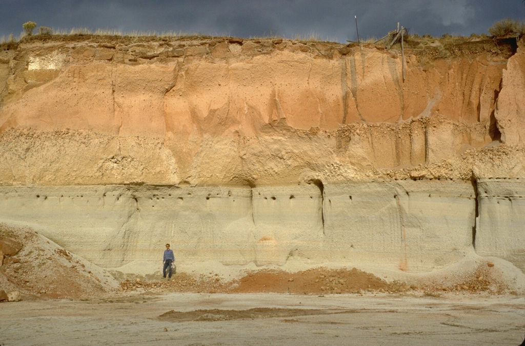 The Mesa Falls Tuff is exposed in a quarry wall near Ashton, Idaho that shows light-colored airfall and pyroclastic-surge deposits overlain by orange-colored pyroclastic-flow deposits.  The 280 cu km Mesa Falls Tuff, deposited about 1.3 million years ago during the second of Yellowstone's three largest eruptions, resulted in the formation of the 16-km-wide Henrys Fork caldera west of Yellowstone National Park. Photo by Lee Siebert, 1994 (Smithsonian Institution).