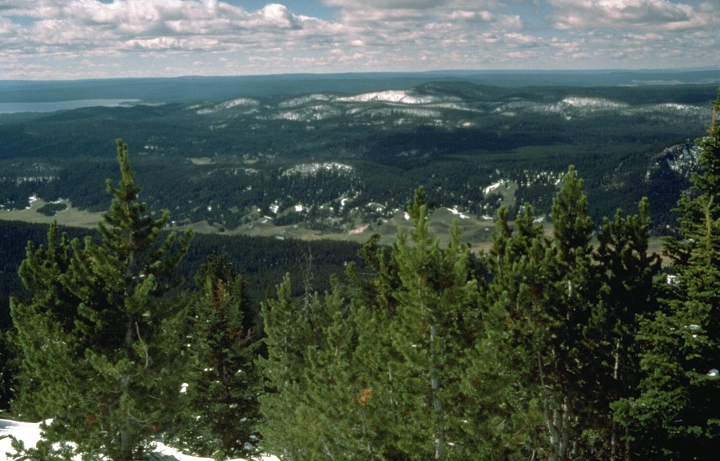 The tip of Yellowstone Lake is seen at the upper left from Pelican Cone near the NE rim of Yellowstone caldera.  The forested, snow-capped peaks in the center are rocks of the Sour Creek resurgent dome, an area of uplifted and faulted post-caldera rocks. Photo by Dzurisin, 1985 (U.S. Geological Survey).