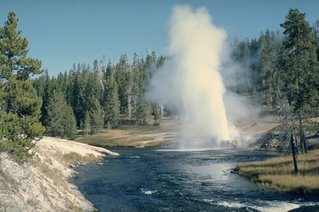 Riverside Geyser in the Upper Geyser Basin is the most regular of Yellowstone's geysers. About every six hours it ejects a 25-m-high inclined jet from a small vent hole on the east bank of the Firehole River 2 km downstream from Old Faithful. Photo by Lee Siebert, 1968 (Smithsonian Institution).