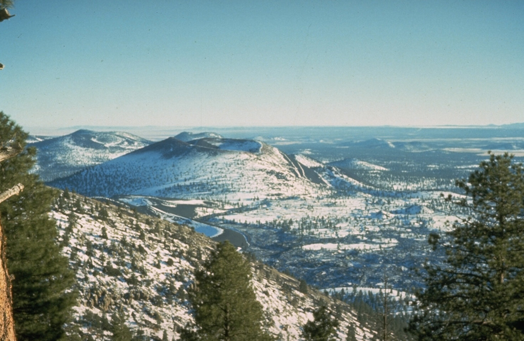 Snow-mantled Sunset Crater (left-center), seen from O'Leary Peak to the NW, is the youngest volcanic feature of the San Francisco Mountain volcanic field, which covers a vast area of northern Arizona between Flagstaff and the Grand Canyon.  The Sunset Crater eruption began about 1100 CE from a chain of cinder cones and vents trending NW-SE, the largest of which is Sunset Crater.  Three lava flows were erupted, the longest of which traveled 11 km to the NE. Photo by Ed Wolfe, 1973 (U.S. Geological Survey).