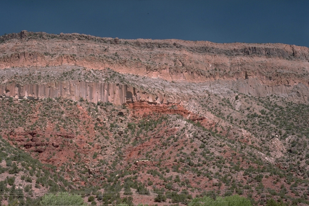 Thick deposits of welded pumice form cliffs along the Jemez River valley SW of  the Valles caldera, capping darker-red, bedded sedimentary rocks at the base of the canyon.  The lowermost pyroclastic-flow deposit, showing pronounced columnar jointing, is the Otowi member of the Bandelier Tuff.  The top of the section is the Tshirege member of the Bandelier Tuff.  The two eruptions, about 1.45 and 1.1 million years ago, ejected about 600 cu km of magma and resulted in the formation of  Valles caldera.   Photo by Lee Siebert, 1989 (Smithsonian Institution).