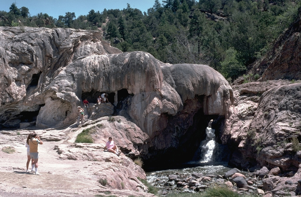 Soda Dam, along the Jemez River, is a travertine dam formed across a gorge in Precambrian granite-gneiss SW of the rim of Valles caldera.  The travertine has been deposited over the past 5000 years by carbonated thermal waters discharged along the Jemez fault zone.  About 15 hot springs related to the Valles caldera thermal system are found at this location. Photo by Lee Siebert, 1989 (Smithsonian Institution).