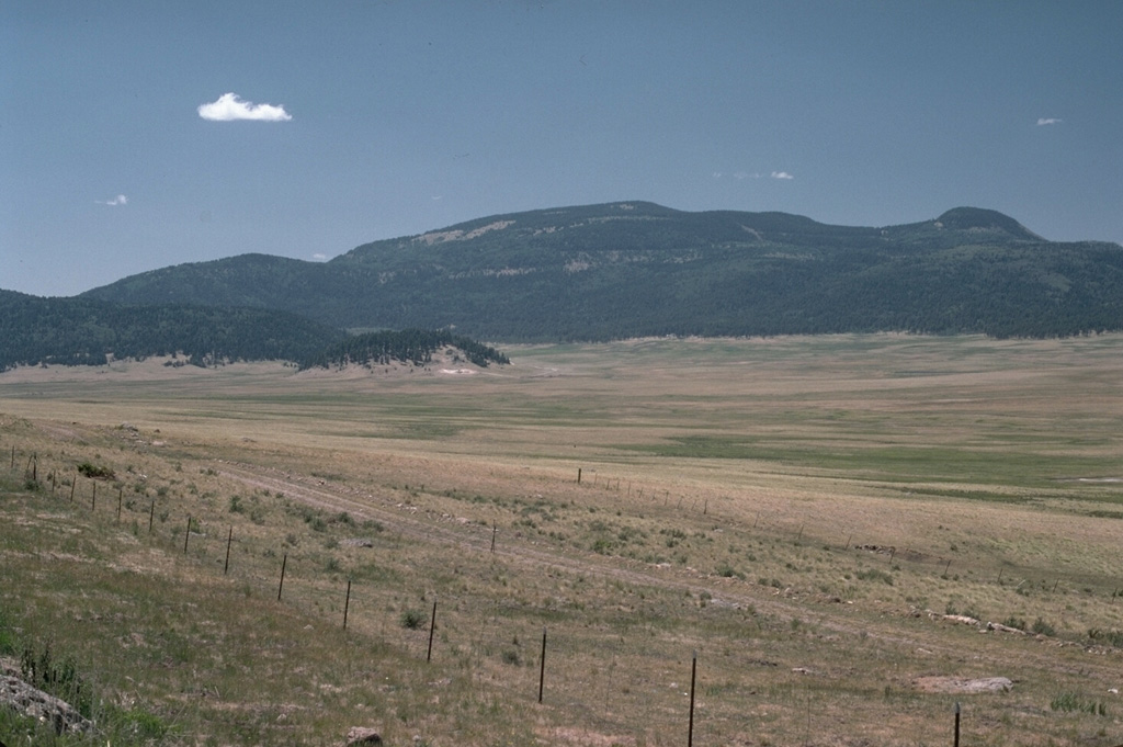 Redondo Peak in the center and Redondito peak on the right are the eastern half of a resurgent dome in the center of the Valles caldera, seen from the SE across the caldera moat, Valle Grande.  The uplifted resurgent dome is formed primarily of densely welded Bandelier Tuff that was uplifted about 50-100,000 years after formation of the caldera.  Cerro La Jara, the small hill on the caldera floor at the middle left, is a small rhyolitic lava dome erupted along ring-fractures.  Photo by Lee Siebert, 1989 (Smithsonian Institution).