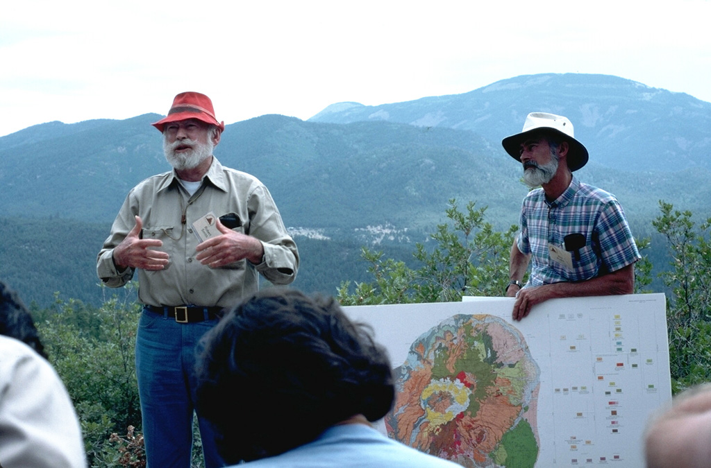 Volcanologists Bob Smith (left) and Roy Bailey (right) lead a geological field trip to Valles caldera.  Redondo Peak at the upper right rises to 3430 m,  840 m above the caldera floor, and along with Redondo Border peak at the center, forms the western half of the uplifted resurgent dome seen at the center of the geologic map.  The down-dropped Redondo Creek graben, which cuts diagonally through the center of the photo, has been the focus of geothermal exploration in the caldera. Photo by Lee Siebert, 1989 (Smithsonian Institution).