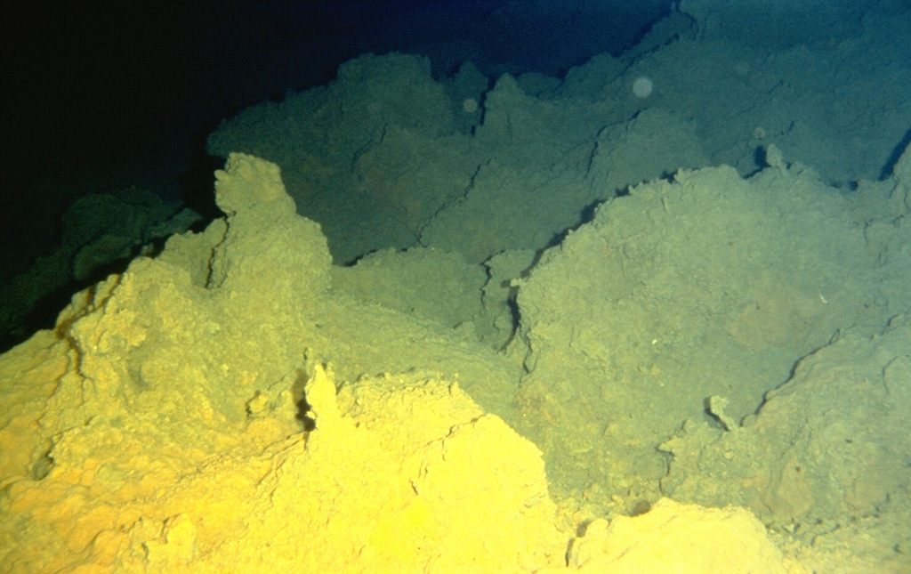 Sulfur deposited from fumarolic vents coats lava flows on Loihi seamount. Loihi, the youngest Hawaiian volcano, rises to within 975 m of the sea surface 35 km off the SE coast of the island of Hawaii. Two rift zones, oriented N-S, give the volcano an elongated form, and prompted its name, which is the Hawaiian word for "long." Fresh, sediment-free lava flows indicate the young age of the submarine volcano, and seismic swarms related to intrusive or eruptive activity have been recorded frequently. Photo by the Hawaii Undersea Research Laboratory (University of Hawaii).