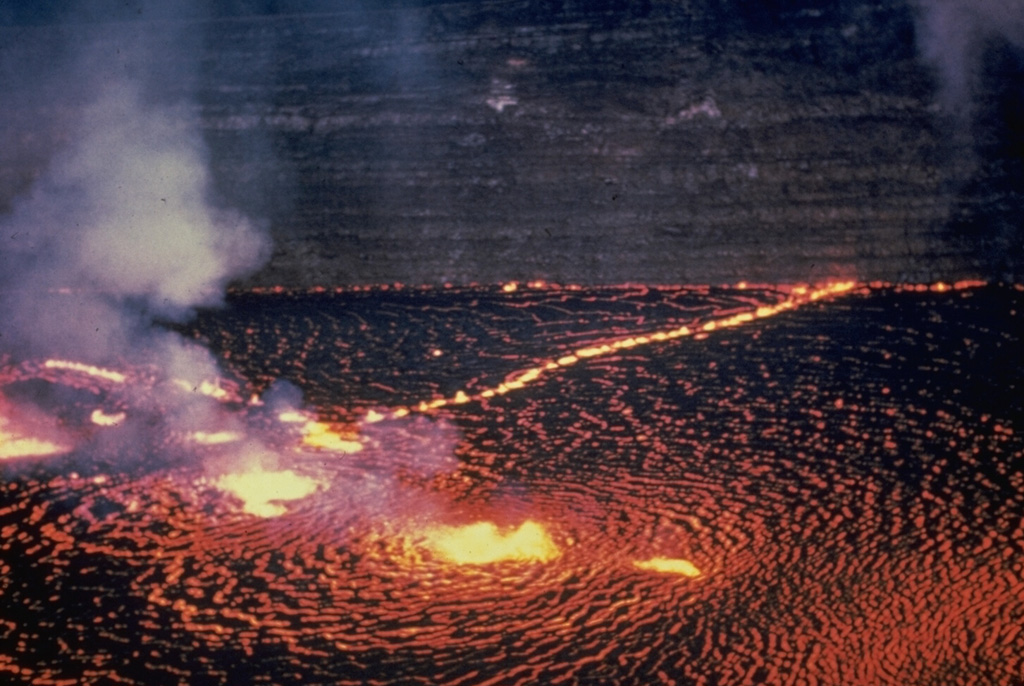 The Halema‘uma‘u lava lake is seen from the east on 31 May 1954. Several areas of vigorous lava fountaining occurred here as well as lower fountaining along nearby fissures. Later in the first day of the three-day-long eruption the fissures extended over the crater wall and to the ENE to produce lava flows on the caldera floor. Thin lava flows exposed in the Halema‘uma‘u pit crater walls appear in the background. Photo by Jerry Eaton, 1954 (U.S. Geological Survey).