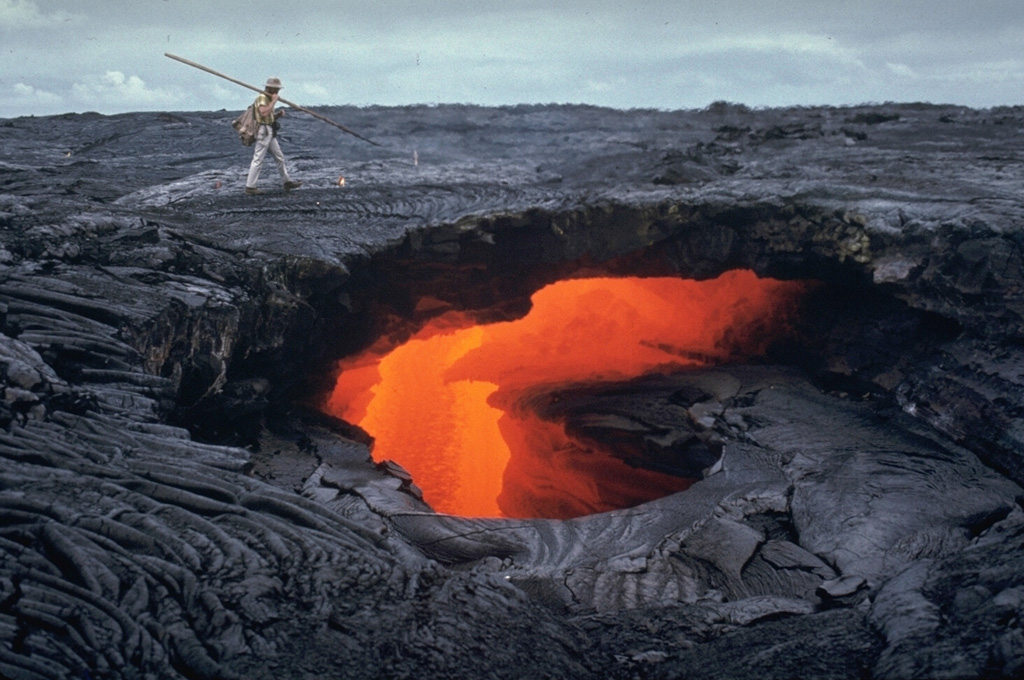 Lava flows are commonly fed through tubes beneath the crusted-over surface of the flow. The ceilings of lava tubes frequently collapse, producing skylights, through which the flowing lava is visible. This 21 October 1970 photo of a lava flow from Mauna Ulu at Hawaii's Kilauea volcano shows several ledges within the lava tube that mark previous levels of flow. The walls and roofs of lava tubes are efficient thermal insulators that allow the lava to travel long distances without solidifying. Some tubes formed during the Mauna Ulu eruption were 11 km long. Photo by Jeffrey Judd, 1970 (U.S. Geological Survey).