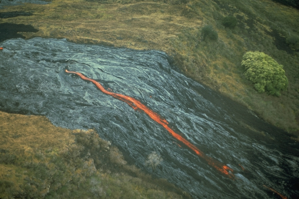 An incandescent lava flow from Mauna Ulu emerges from a lava tube and descends the Poliokeawe Pali cliff on 1 January 1973. Lava flows traveled 12 km to reach the coast over a 9-km-wide front during the 1969-74 eruption. Photo by Don Peterson, 1973 (U.S. Geological Survey).