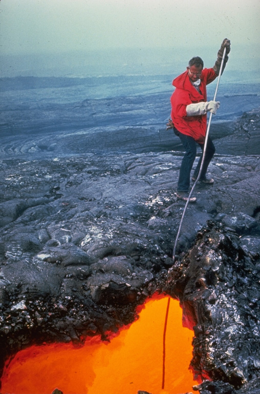 A volcanologist from the Hawaiian Volcano Observatory extracts a sample of fresh lava from an active lava tube during the 1969-74 Mauna Ulu eruption. Asbestos gloves were used for protection against the intense radiant heat. Sampling at various stages of an eruption is used to determine changes in the chemistry and mineralogy of erupted lavas. Photo by Bob Tilling, 1973 (U.S. Geological Survey).