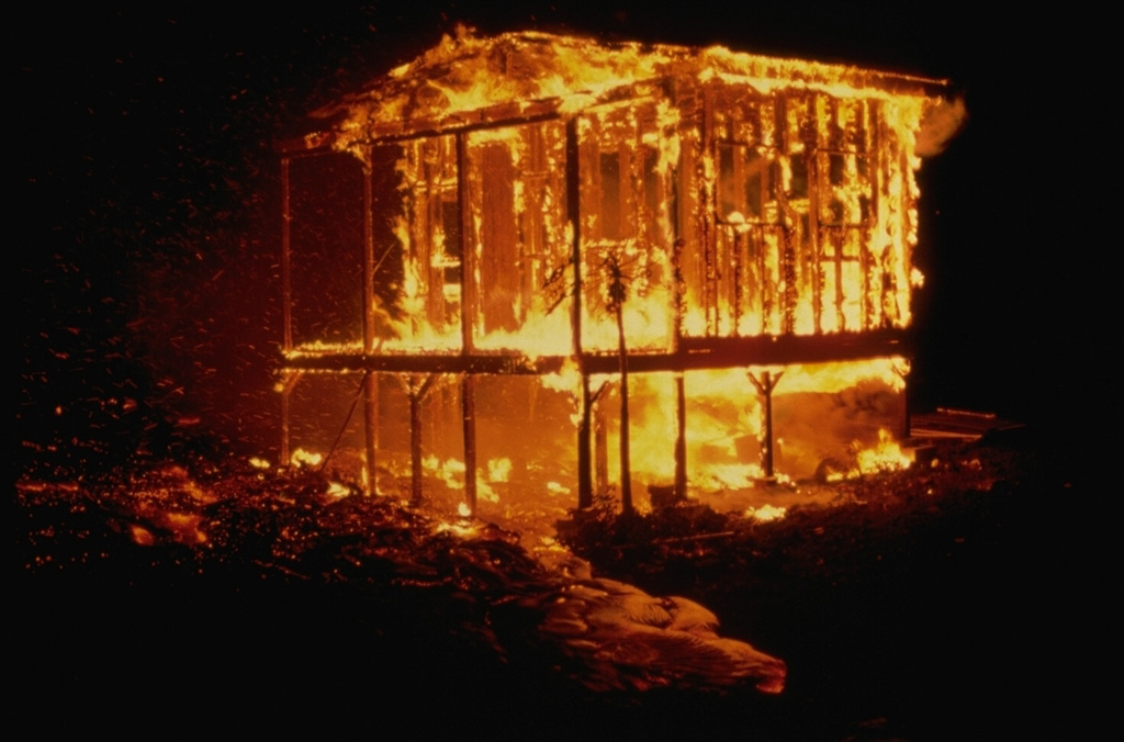 A house near Hawaii's Puna coast burns in May 1987, one of many ignited by lava flows from Kilauea's long-term east rift zone eruption.  Lava flows overran the coastal village of Kalapana in 1990 and buried the popular black sand beach at Kaimu.  Although some houses were removed before the housing lots were overrun, more than 75 houses were destroyed by lava flows in 1990. Copyrighted photo by Katia and Maurice Krafft, 1987.