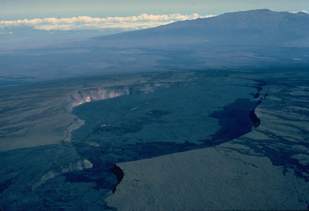 Calderas at the summits of basaltic shield volcanoes, such as this one at Hawaii's Mauna Loa volcano differ from those formed at more silicic stratovolcanoes.  The 2.4 x 4.8 km wide Mokuaweoweo caldera, seen here from the south with Mauna Kea volcano in the background, formed when the summit collapsed after large amounts of magma were siphoned away from the summit region by flank eruptions or lava intrusions.  The elongate, scalloped form of the caldera reflects both the influence of rift systems and the incremental growth of the caldera. Copyrighted photo by Katia and Maurice Krafft, 1984.