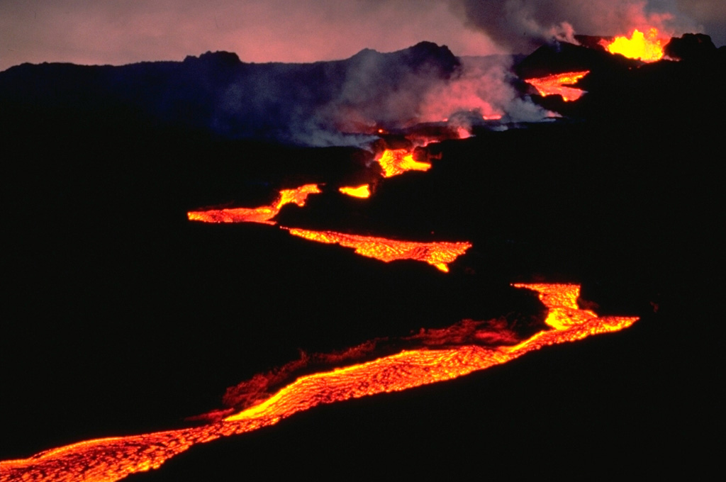 An incandescent lava flow winds its way down the NE rift zone of Mauna Loa volcano early in the morning of March 25, 1984.  The flow direction varies as the lava flow detours around higher areas and follows topographic lows along the broad crest of the NE rift zone. Copyrighted photo by Katia and Maurice Krafft, 1984.